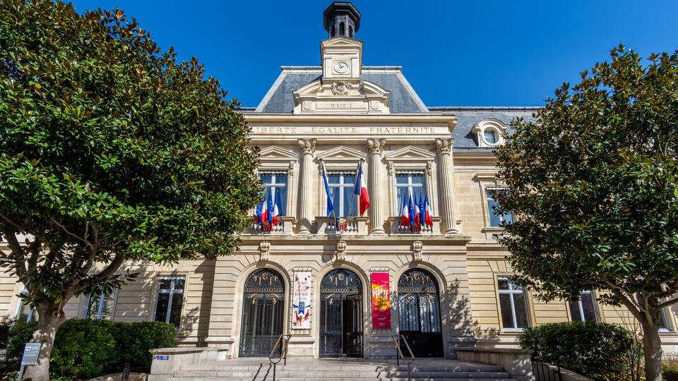 A historic building with classical architecture, featuring a clock tower, columns, and flags.