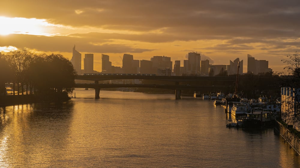 A sunset over a city skyline with a bridge and boats on the water.