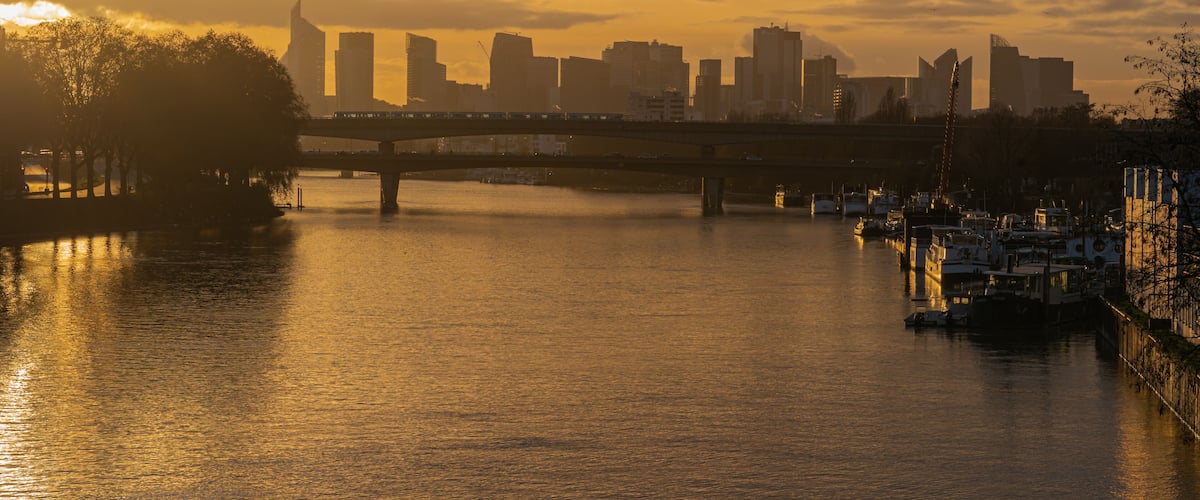 A sunset over a city skyline with a bridge and boats on the water.