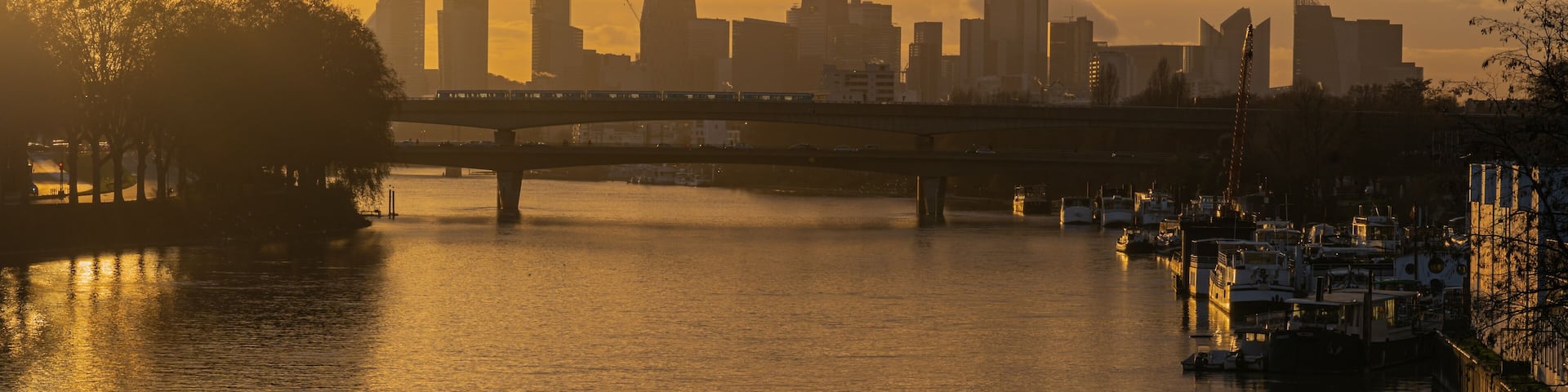 A sunset over a city skyline with a bridge and boats on the water.
