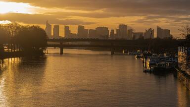 Un atardecer sobre el horizonte de una ciudad, con un puente y barcos en el agua.