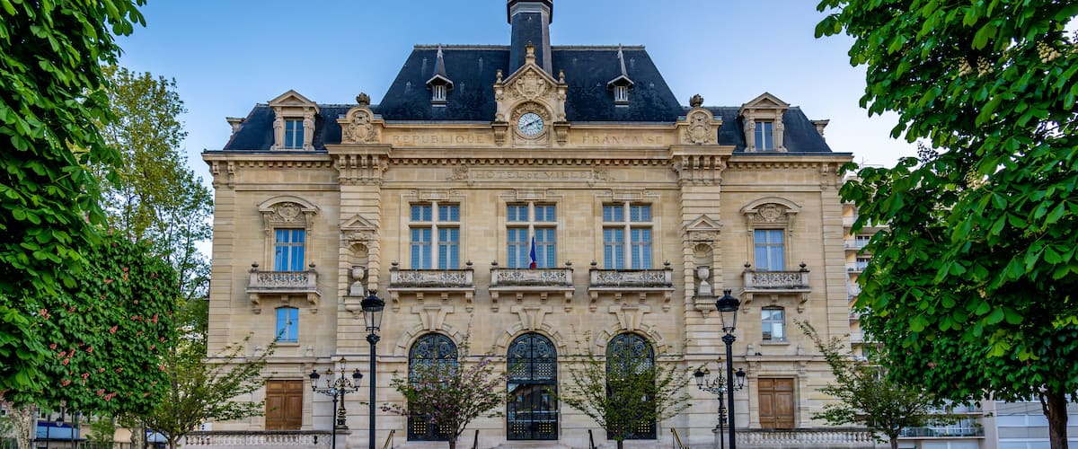 A historic building with a clock tower, ornate architecture, and a well-maintained garden.