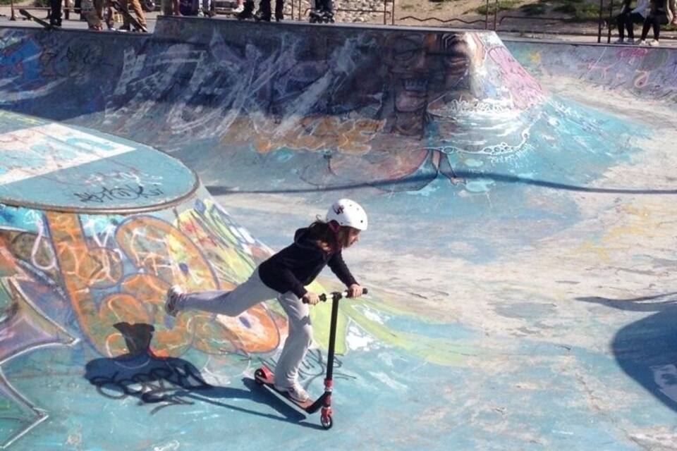 Uma pessoa andando de scooter em um parque de skate com grafites nas rampas.