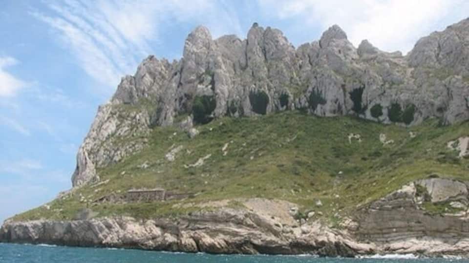Une côte rocheuse, avec une falaise imposante et une petite colline à la végétation clairsemée.