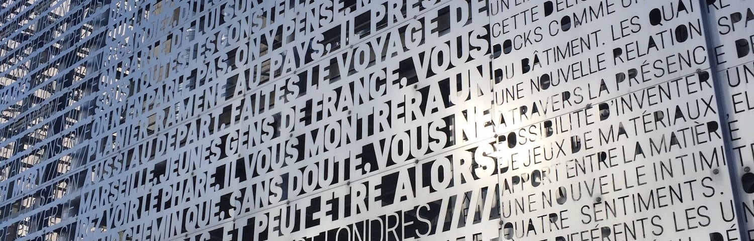 Parede de metal com letras recortadas formando frases em francês.
