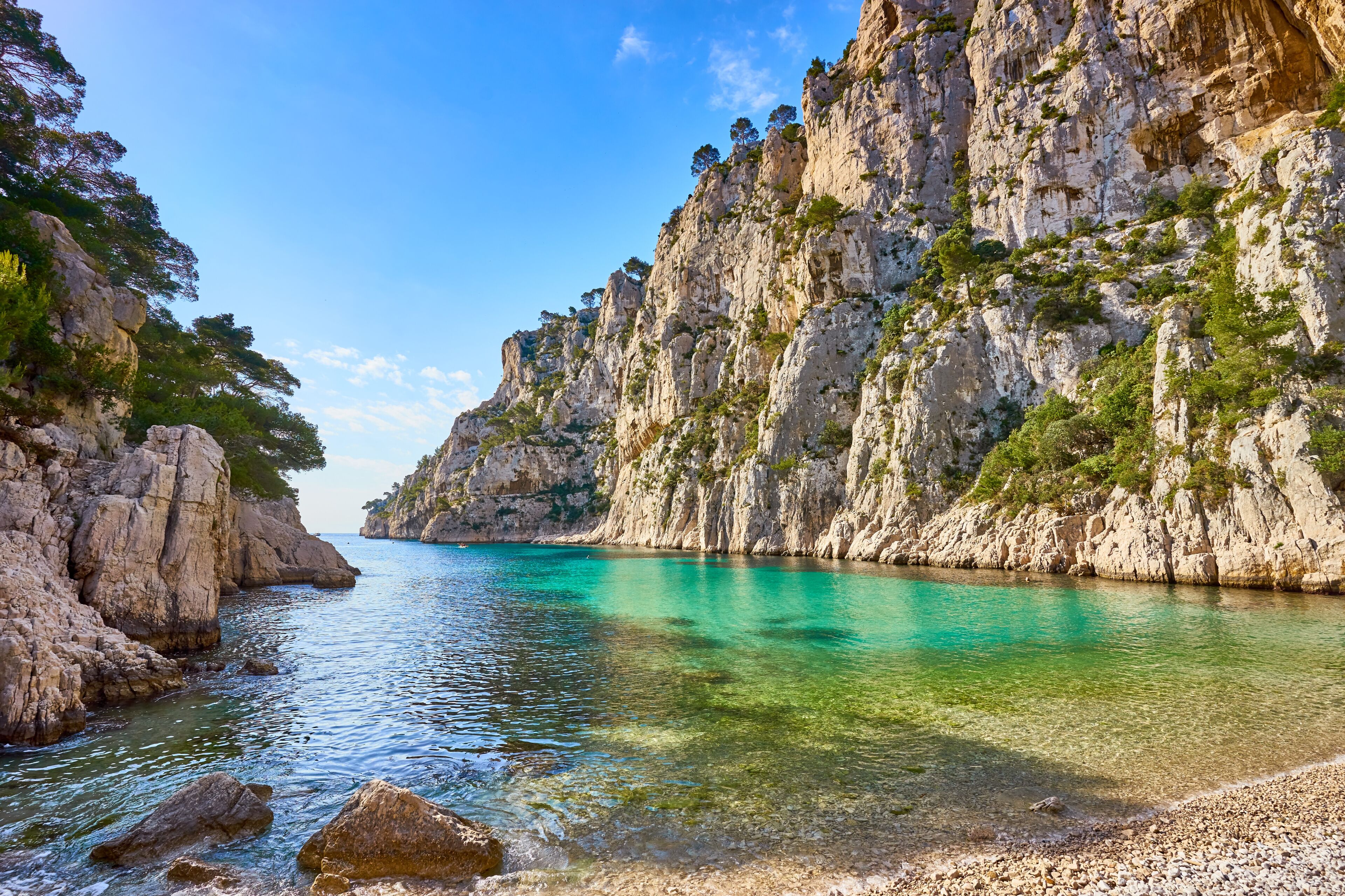 A coastal landscape with clear turquoise water, rocky cliffs, and sparse vegetation.