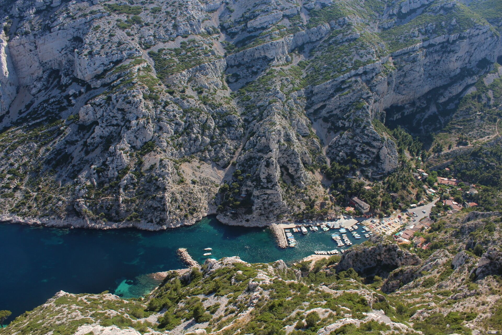 A rugged mountainous landscape with a coastal area featuring a marina with boats docked.