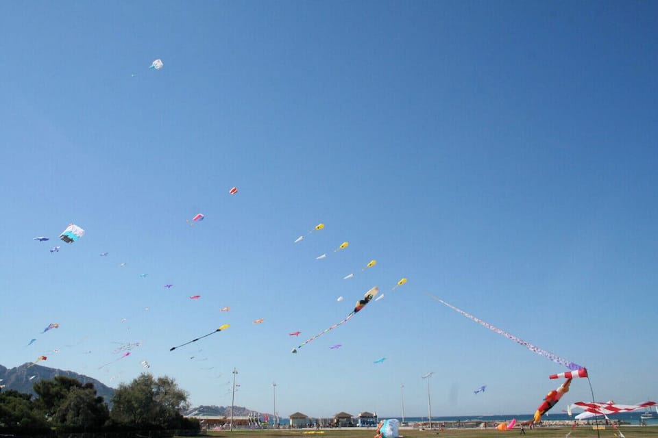 A clear blue sky with numerous kites flying at a beach.
