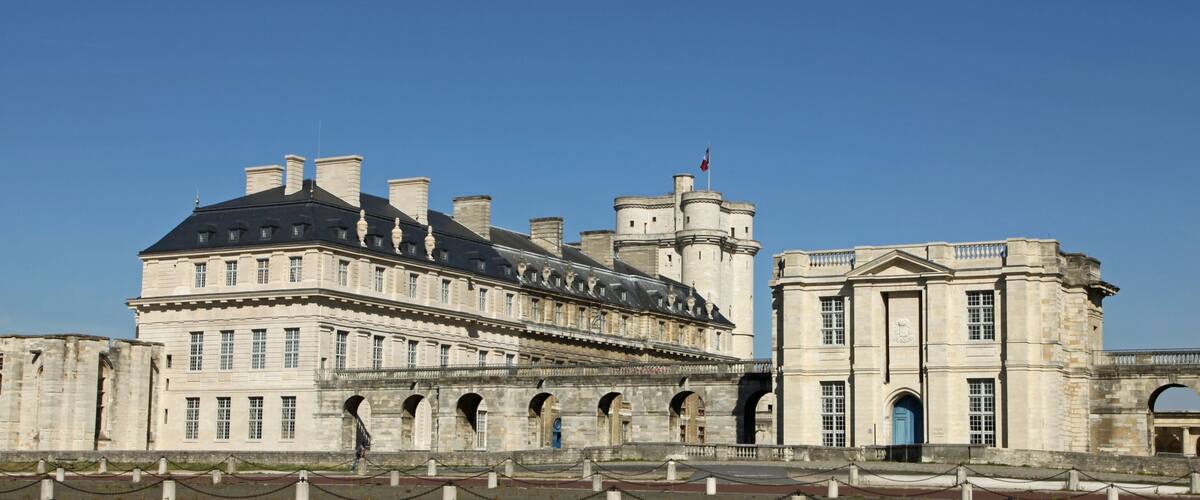 A historic building with a large central tower, multiple arches, and a flag on top.