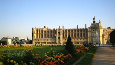 A large historic building with a symmetrical facade, a central courtyard, and a well-maintained garden with colorful flowers.