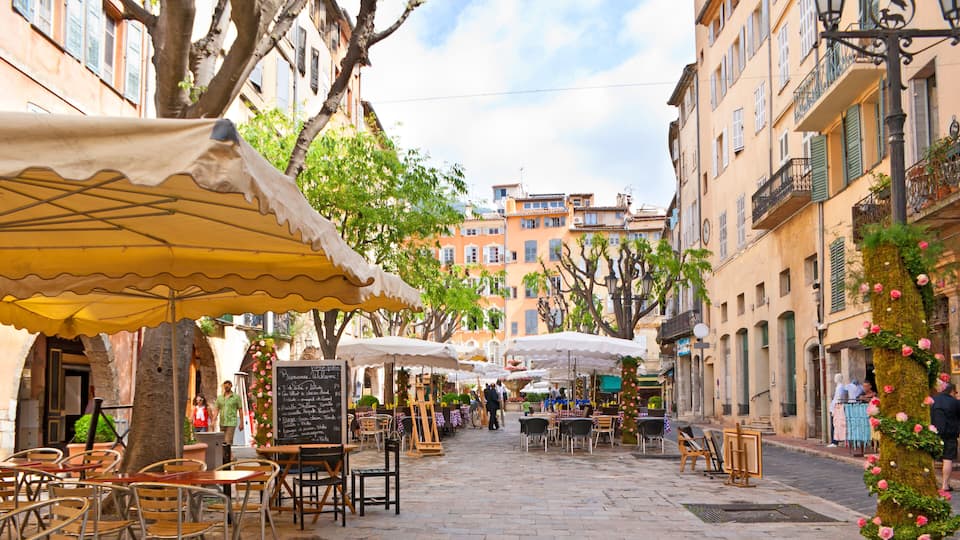 A cobblestone street with outdoor cafes, trees, and historic buildings.