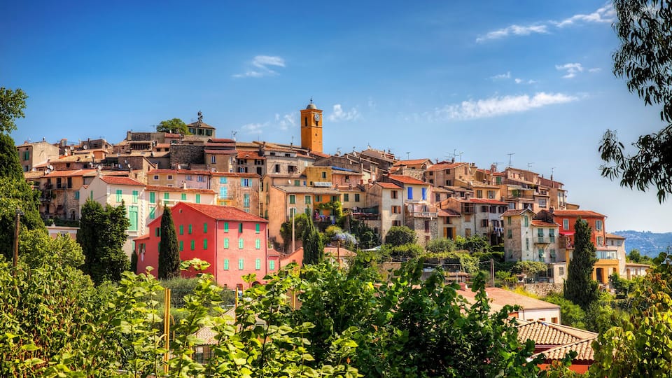 A historic town with colorful buildings, a prominent clock tower, and lush greenery.