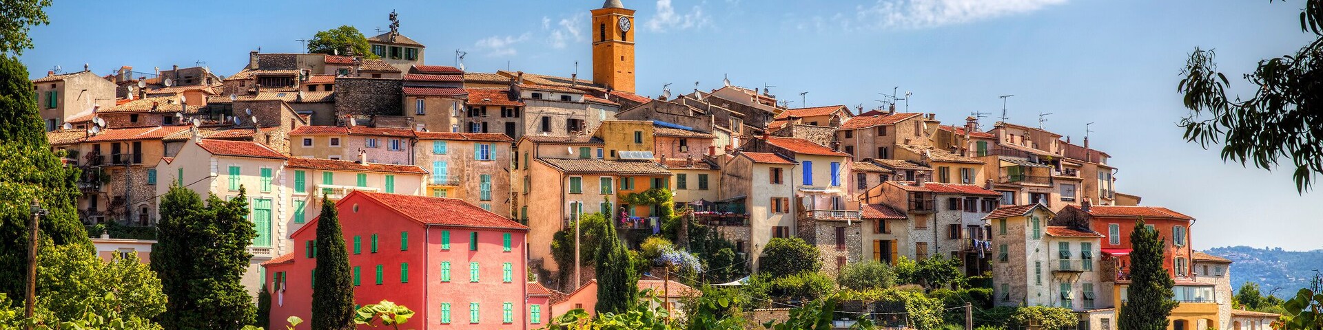 Un pueblo histórico con edificios coloridos, una imponente torre del reloj y abundante vegetación.