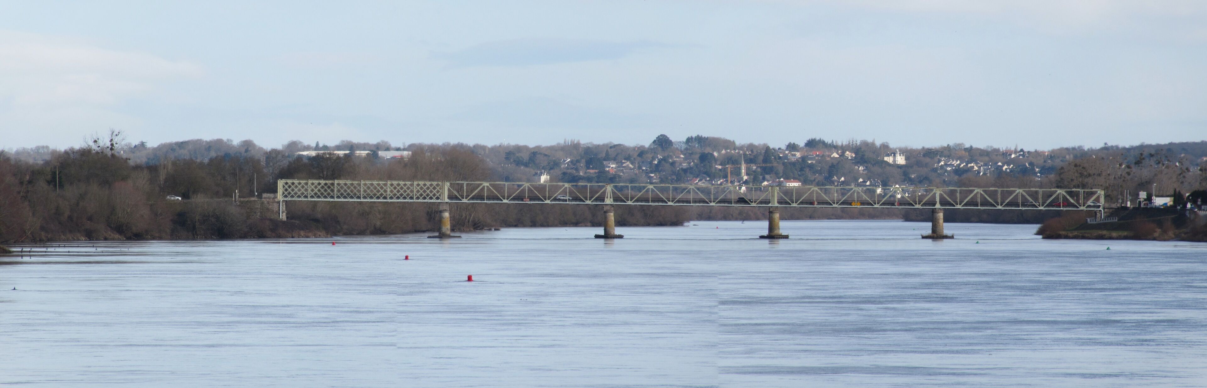 A steel bridge over a calm river with a town in the background.
