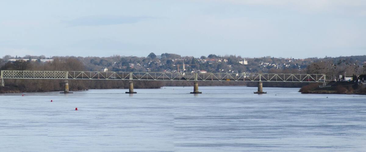 A steel bridge over a calm river with a town in the background.