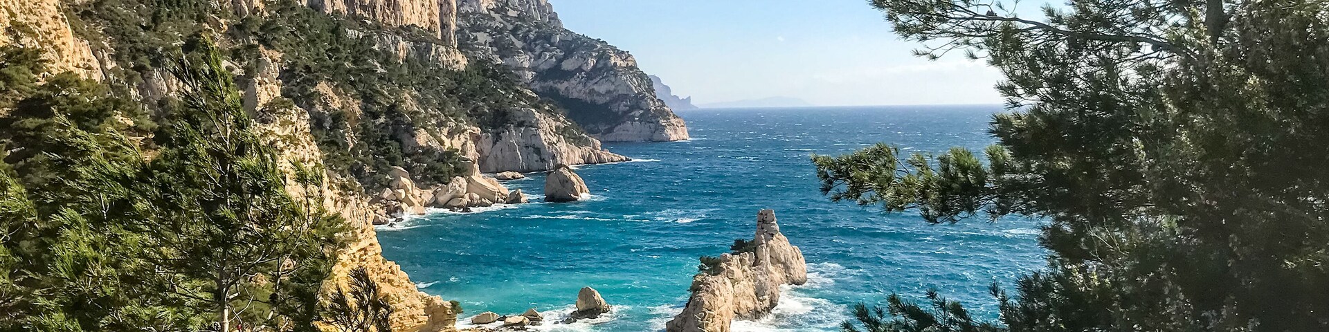Paisaje costero con acantilados rocosos, mar turquesa y pinos.
