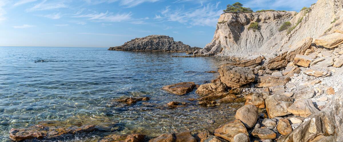 A rocky coastline with clear water, a prominent rock formation, and a cliff with sparse vegetation.