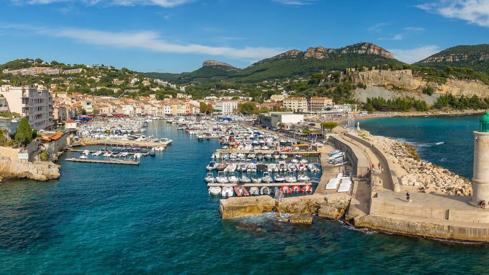 A coastal town with a marina, boats, a lighthouse, and a mountainous backdrop.