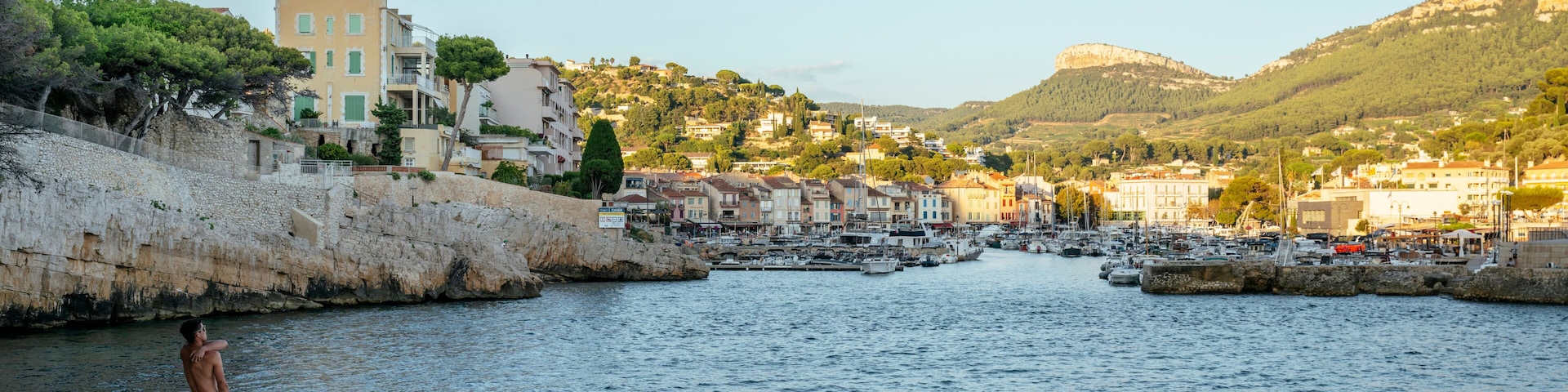 Un pueblo costero con un puerto deportivo, muros de piedra y edificios con balcones.
