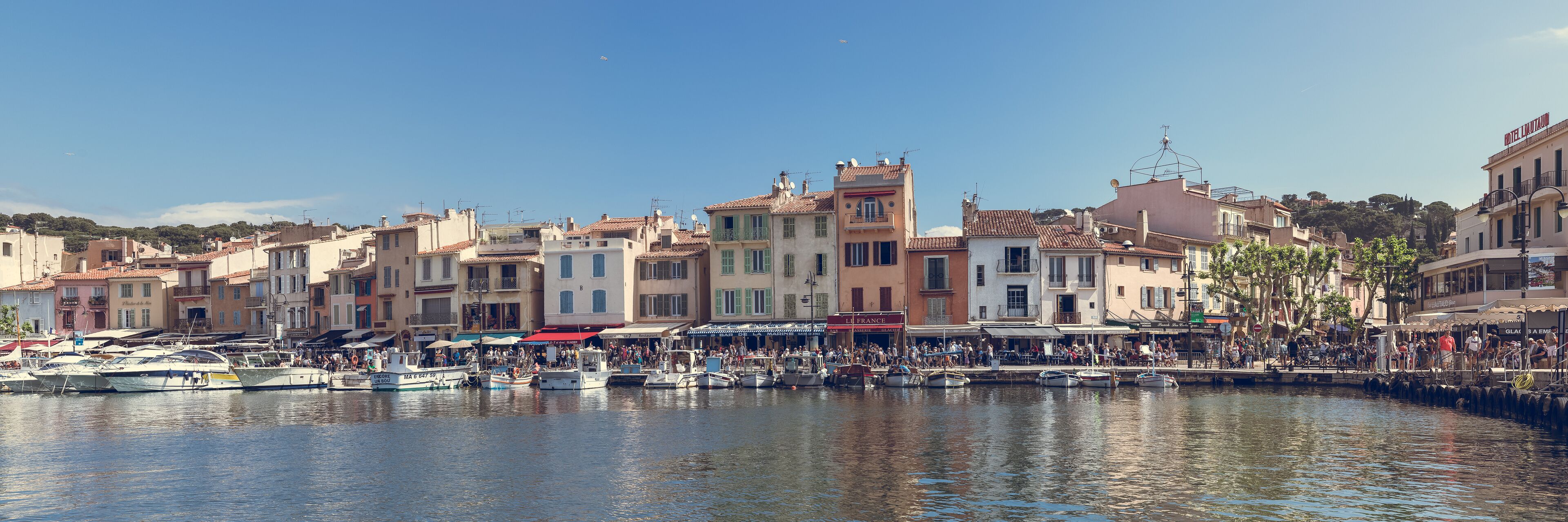 A harbor with boats docked, a crowd of people, and buildings with balconies.