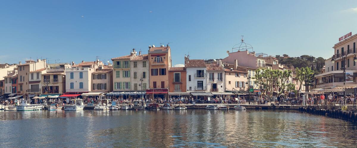 Un port où des bateaux sont amarrés, une foule de personnes et des bâtiments dotés de balcons.