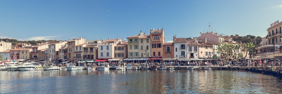 A harbor with boats docked, a crowd of people, and buildings with balconies.