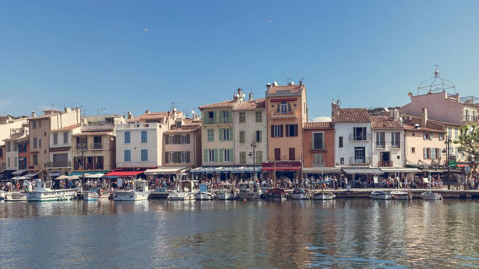 A harbor with boats docked, a crowd of people, and buildings with balconies.