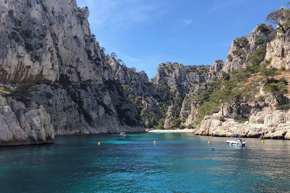 Una cala costanera amb aigües turqueses cristal·lines, penya-segats rocosos i un petit vaixell a la distància.