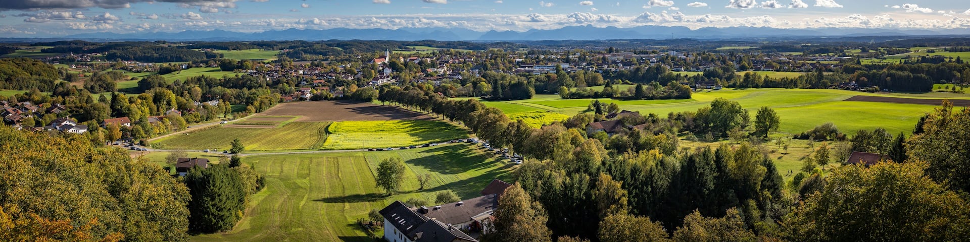 A panoramic view of a town nestled in a valley with rolling hills, a church, and expansive green fields.