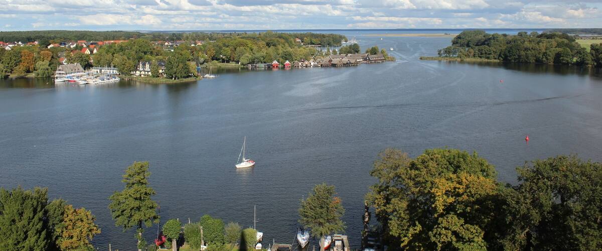 A lake with a sailboat, surrounded by trees and houses.