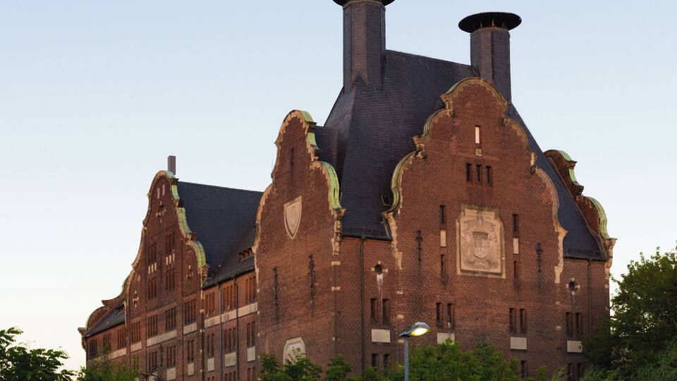 A large brick building with a steeply pitched roof and two chimneys.