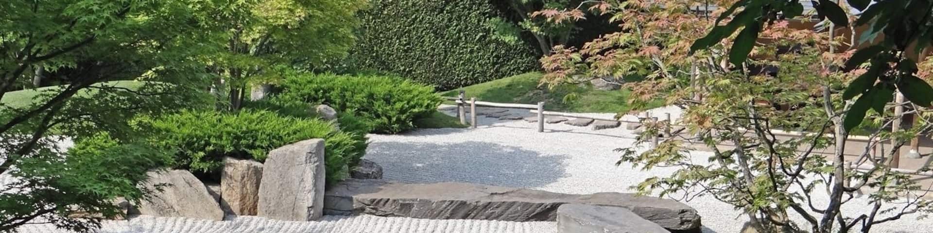 A traditional Japanese garden with a gravel path, rocks, and greenery.