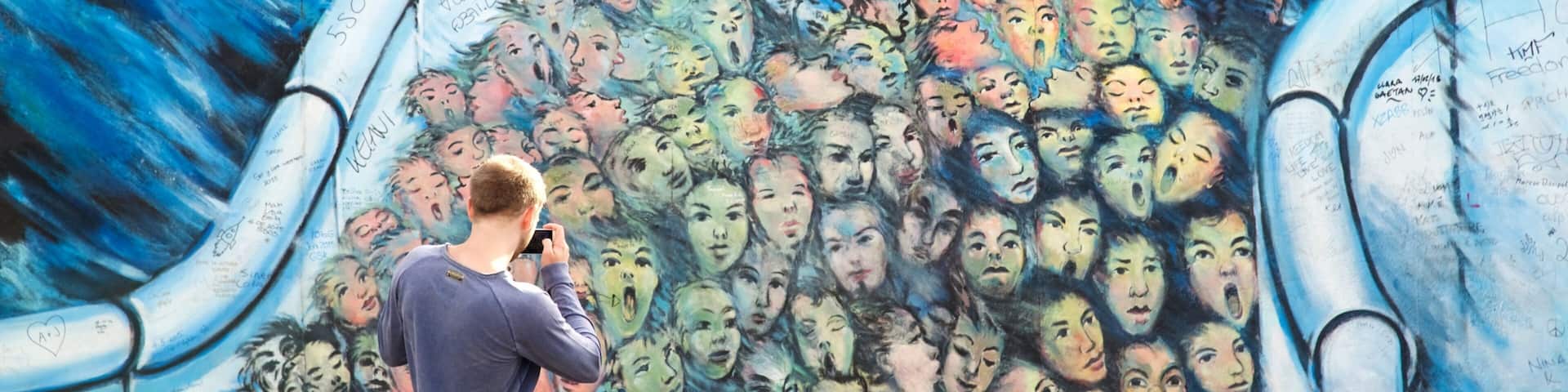 A person taking a photo of a mural with multiple faces.