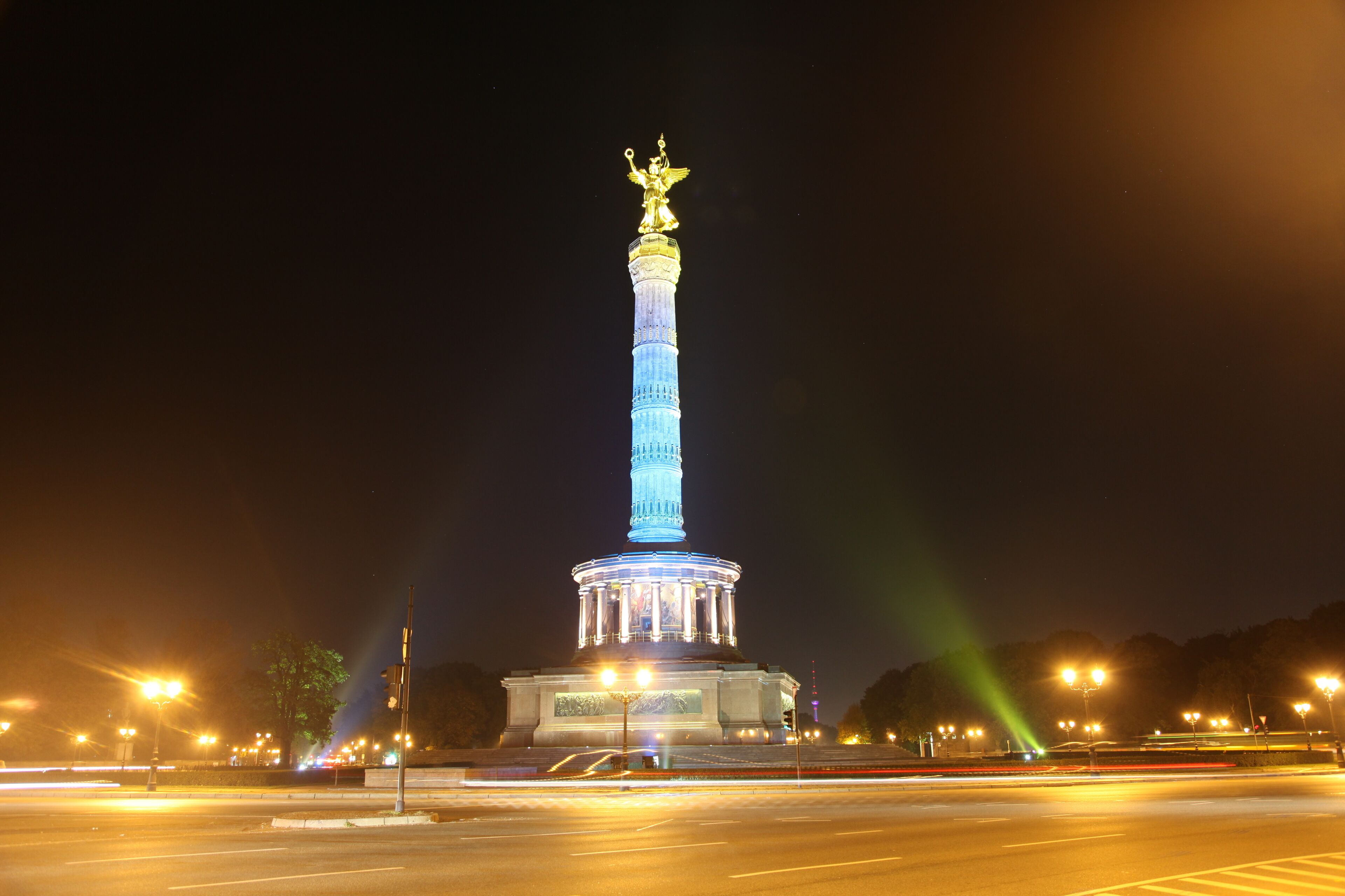 Um monumento bem iluminado com uma estátua no topo, rodeado por postes de luz e um céu noturno limpo.