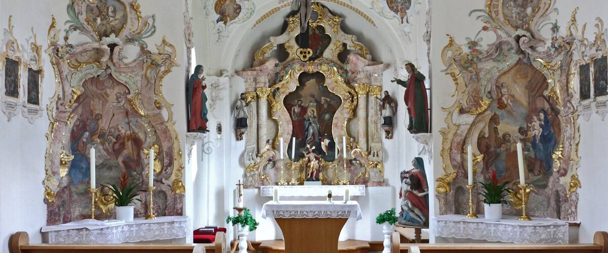 An ornate church interior with detailed frescoes, a central altar, and wooden pews.