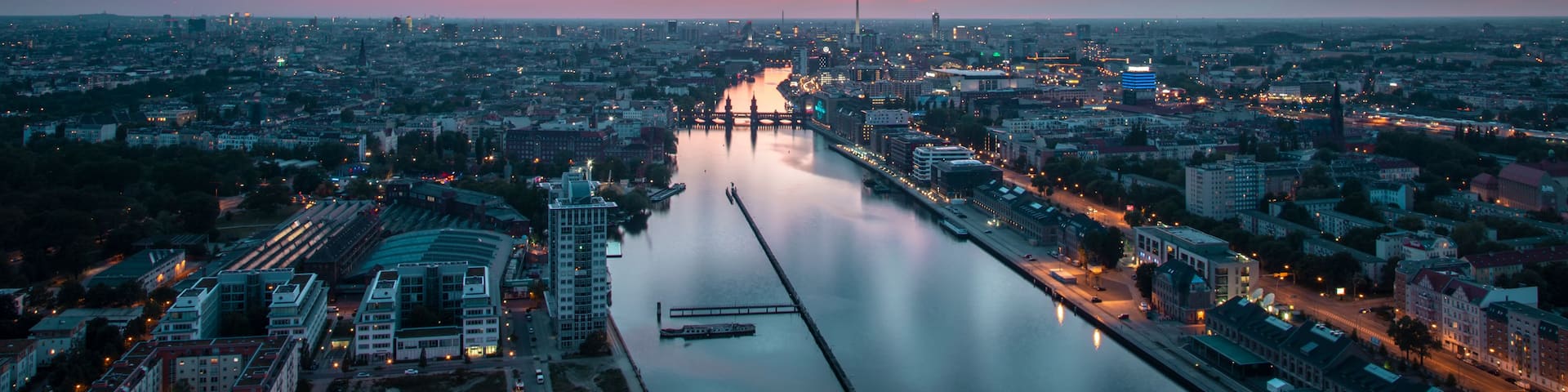 A cityscape at dusk with a river in the foreground and a prominent tower in the distance.