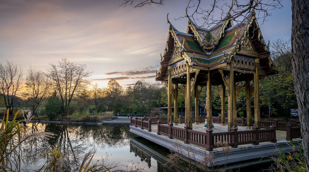 A traditional pavilion with ornate golden roof and columns, surrounded by a calm pond and trees.