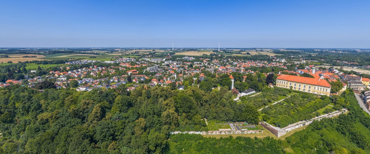 A town with red-roofed buildings, a large green park, and a prominent white tower.