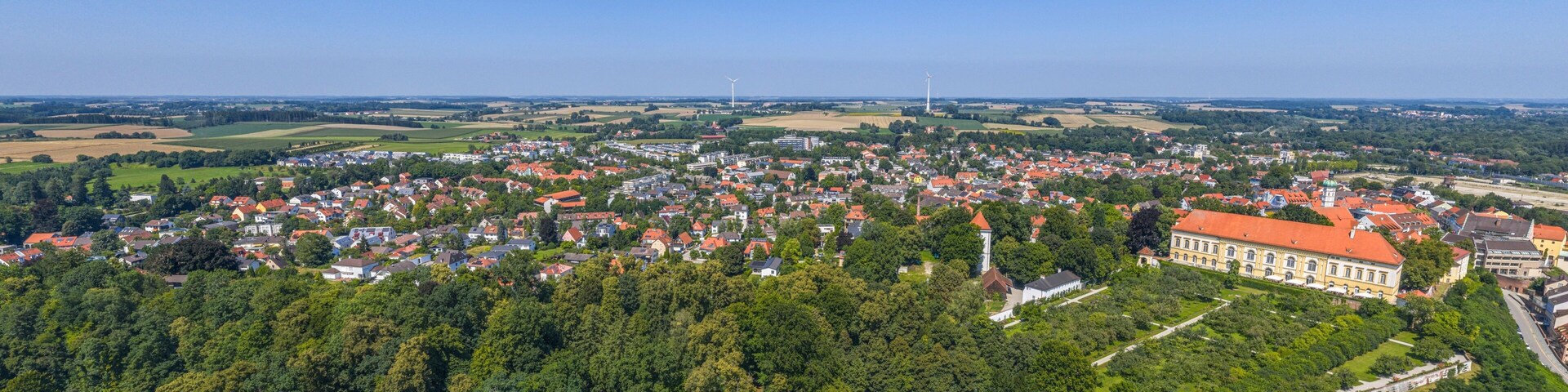 A town with red-roofed buildings, a large green park, and a prominent white tower.