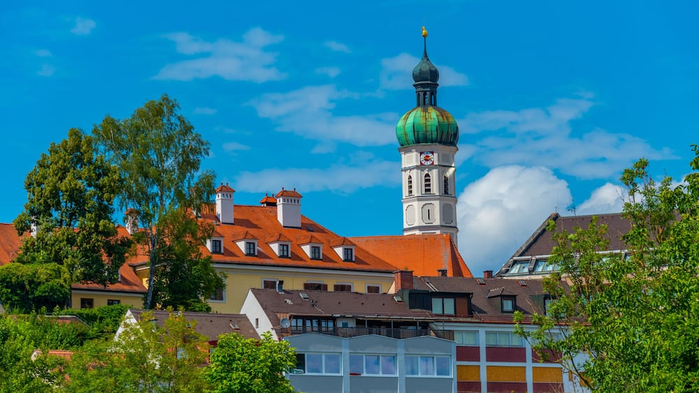 Eine Stadt mit einem markanten Kirchturm, bunten Gebäuden und üppigem Grün.