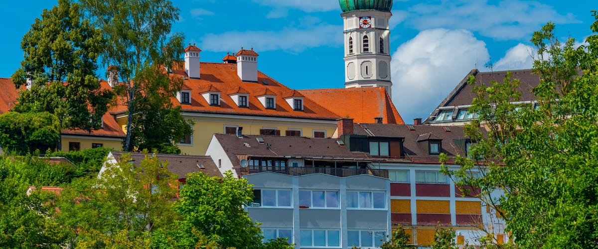 A town with a prominent church tower, colorful buildings, and lush green trees.