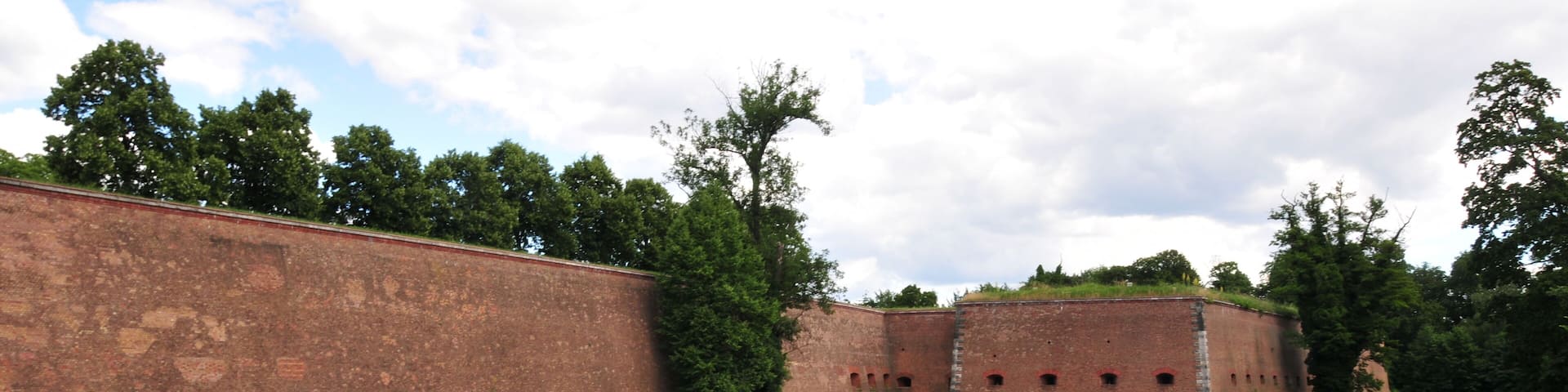 Das Bild zeigt die rechte Seite vom Haupttor der Spandauer Zitadelle in Berlin Spandau, Deutschland. Zu sehen ist auch etwas vom Zitadellengraben bei Windstille an einem sonnigen Tag.