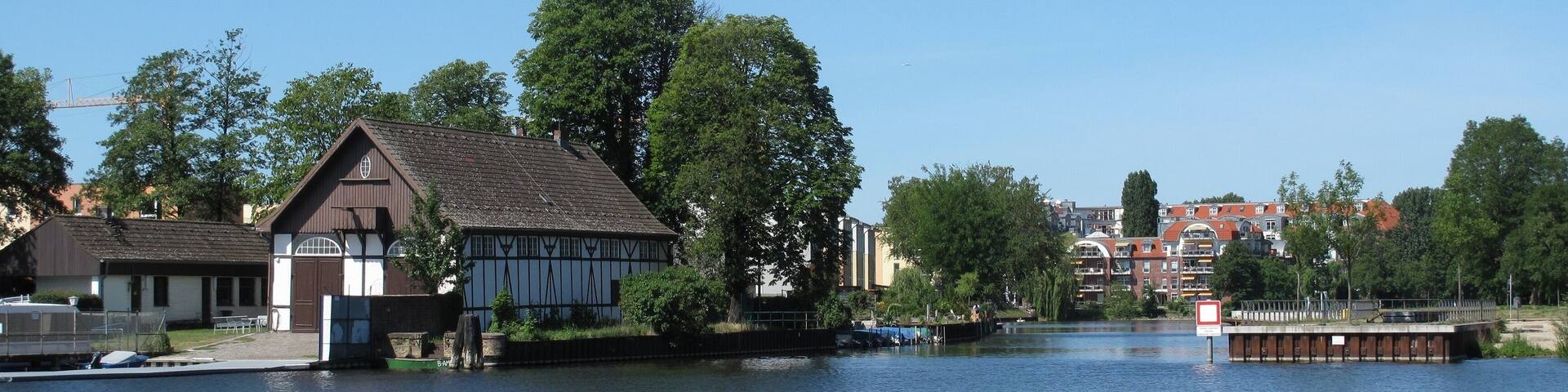 A riverside view with traditional buildings, a wooden dock, and a bridge in the background.