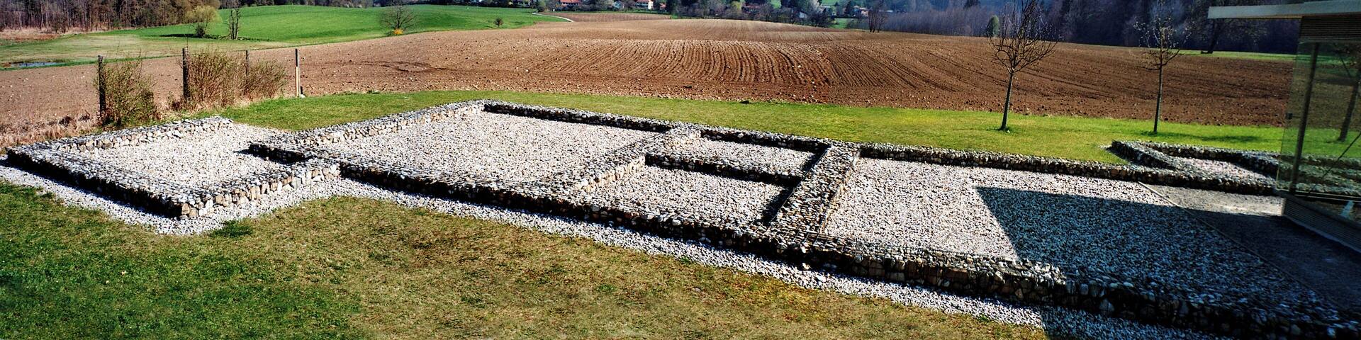 Außenbereich der Villa Rustica in Leutstetten, Landkreis Starnberg, Oberbayern. Im Hintergrund das Dorf Leutstetten. Der Grundriß ganz links gehörte zu einem Keller.