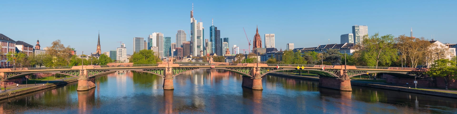 A city skyline with modern skyscrapers, a historic church, and a bridge over a river.