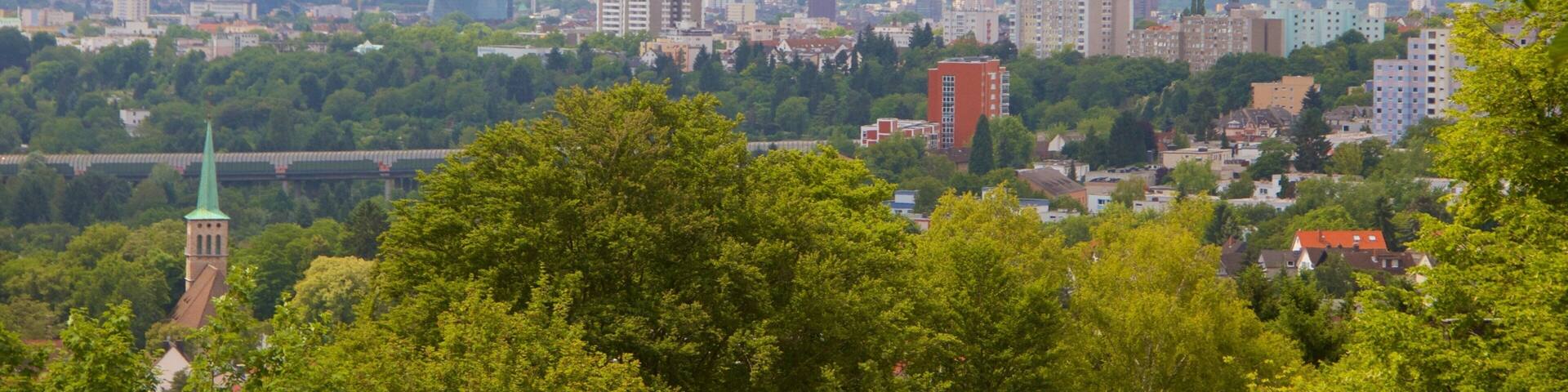 A cityscape with a prominent skyscraper, surrounded by greenery and smaller buildings.
