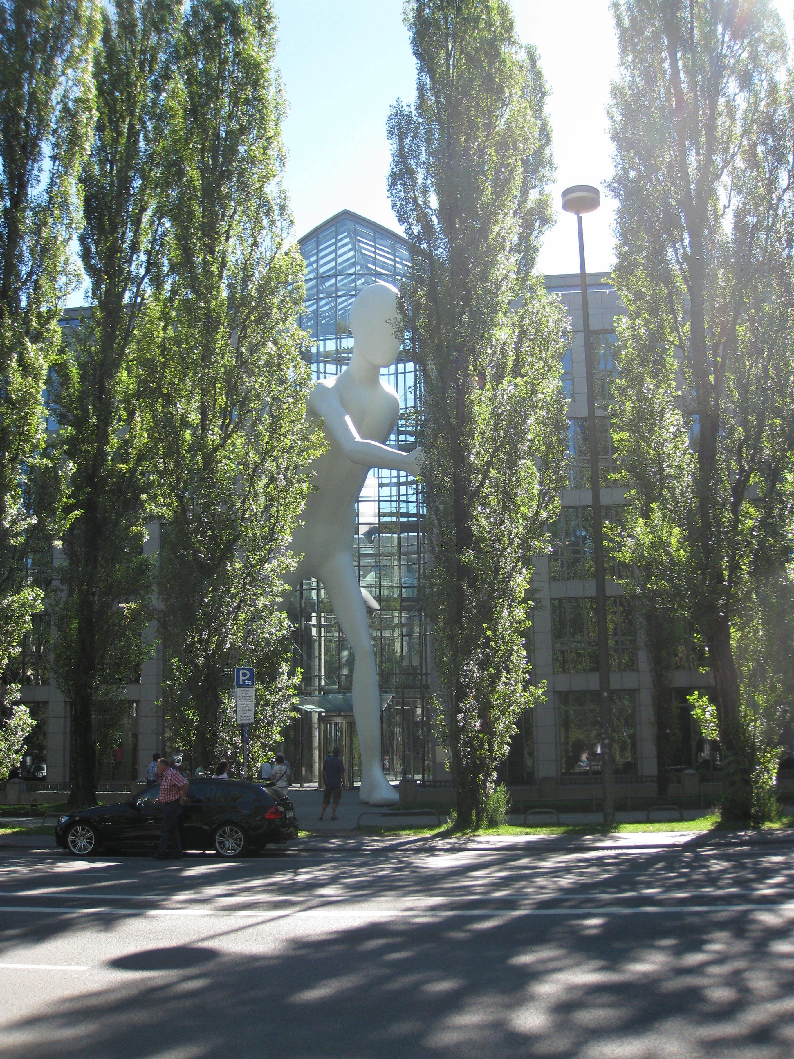 A large white sculpture in a park with trees and a modern building in the background.