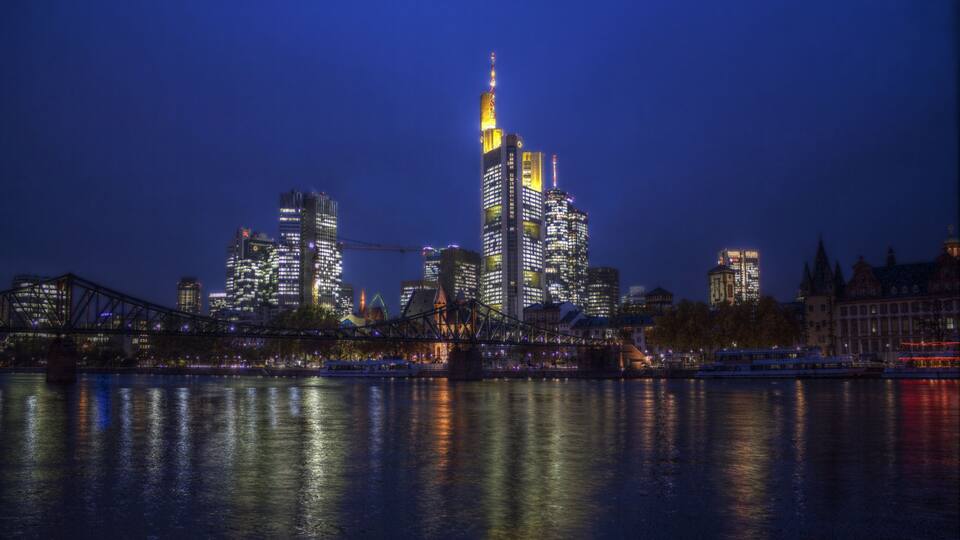 Een verlicht stadsbeeld bij nacht, met glinsterende wolkenkrabbers in het water.
