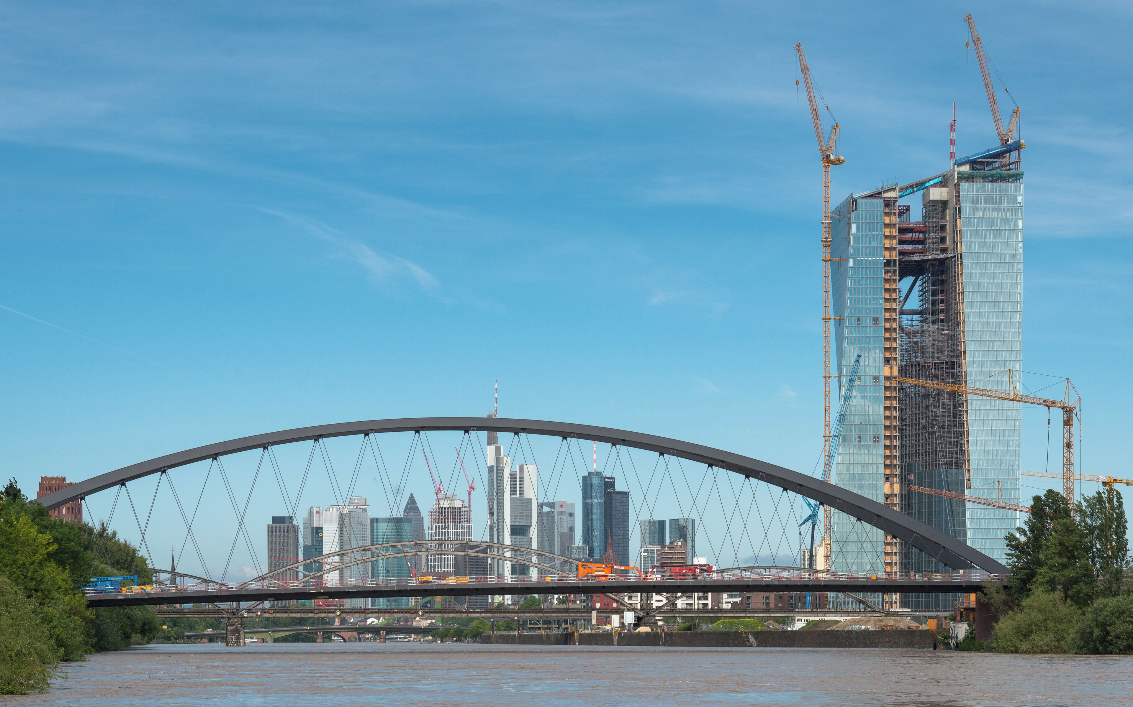 Un pont enjambant une rivière, avec la silhouette d’une ville en arrière-plan et un grand immeuble en construction.