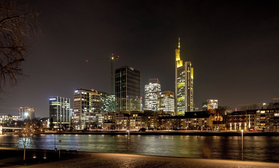 Une vue nocturne d’une ville, avec des gratte-ciel illuminés le long d’une rivière.